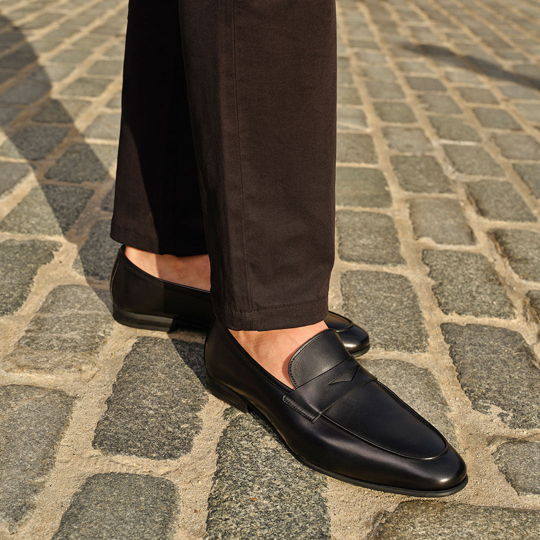 Secondary slide Man in a black pants wearing To Boot's Keats Black Calf Leather Loafer standing on a cobblestone street.